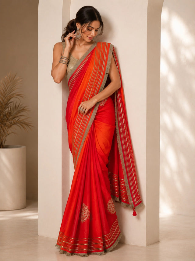 Woman elegantly draped in a vibrant red and orange ombre saree with silver borders.